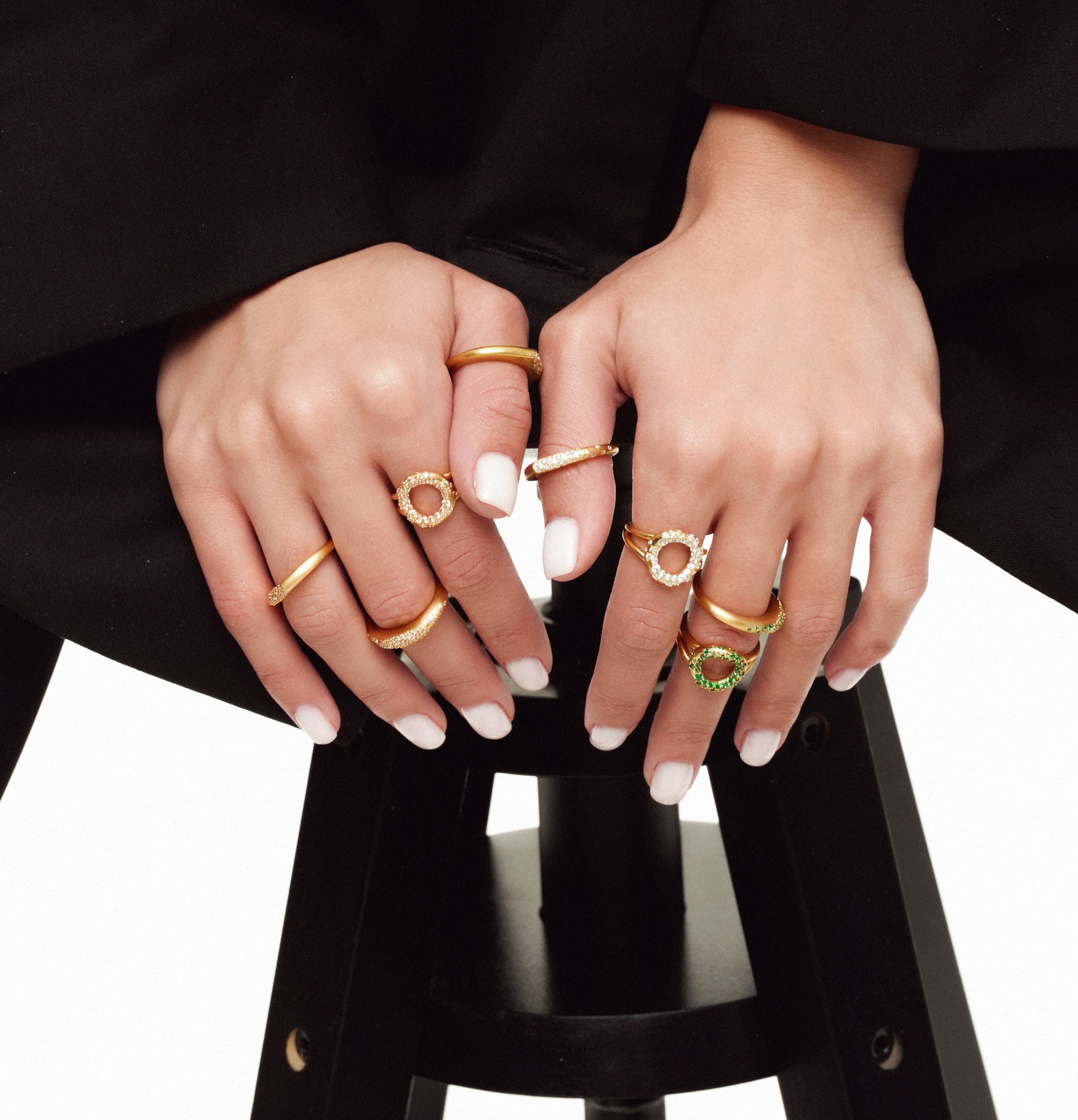 Close-up of hands wearing multiple gold rings on a black background